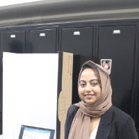A student standing next to a laptop and poster board.